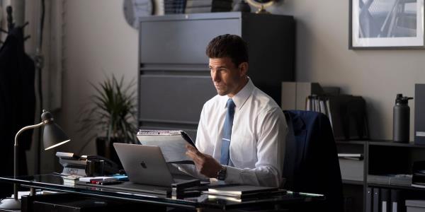 Joshua looks at his calendar while sitting at his desk in The Hating Game.